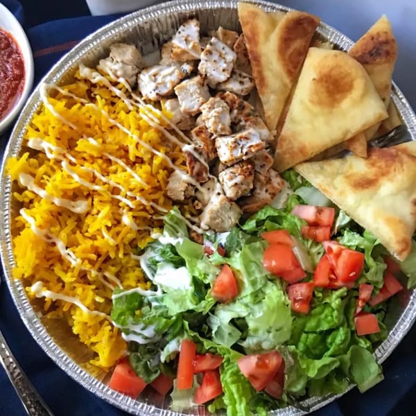 Deli platter with yellow rice, grilled chicken, fresh salad, and pita bread in a foil container.